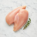 Two raw boneless chicken cutlets on a white marble surface