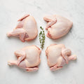 Raw chicken cut into four quarters around a thyme sprig on white marble