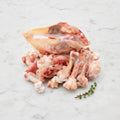 Pile of raw chicken bones and frames with a thyme sprig on white marble