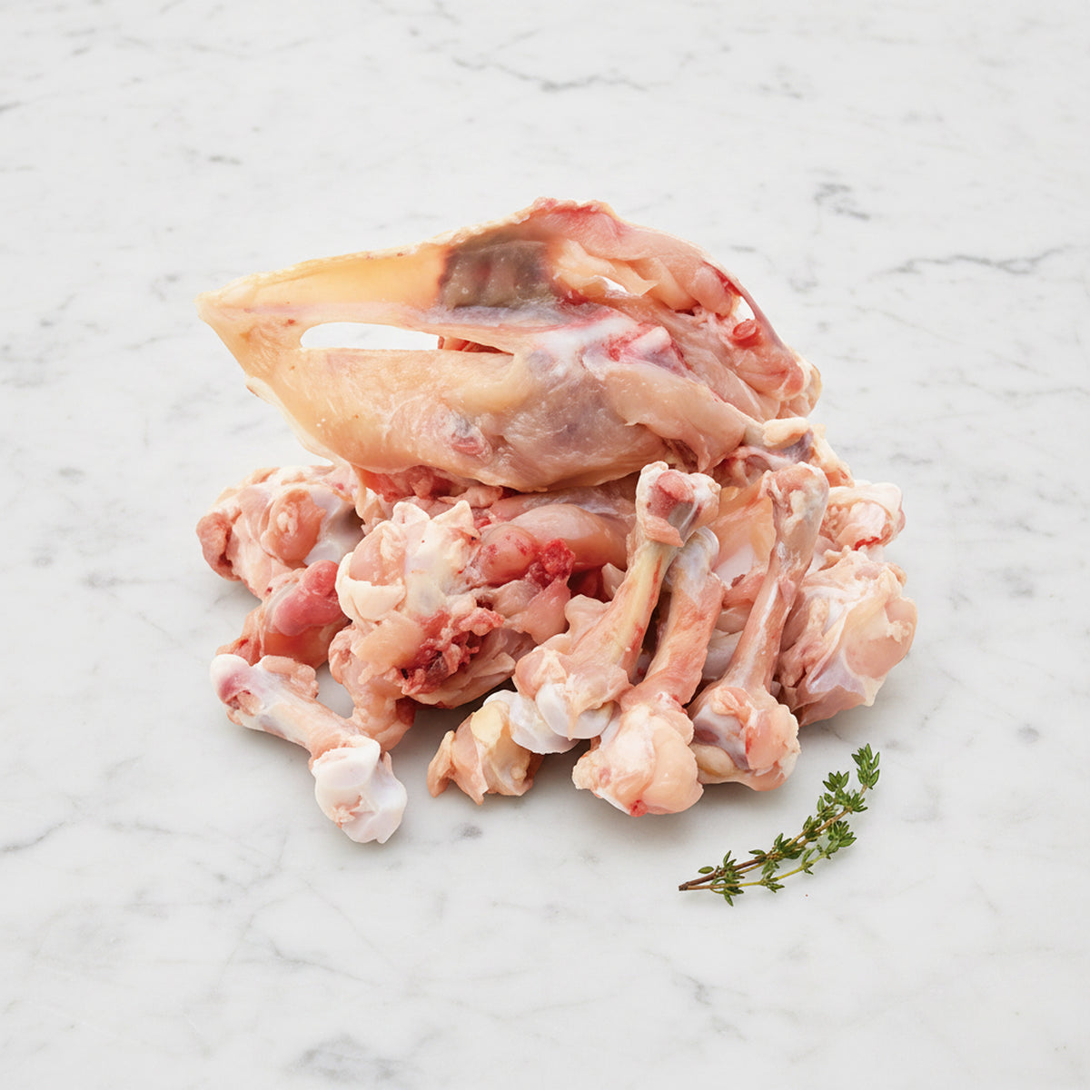Pile of raw chicken bones and frames with a thyme sprig on white marble