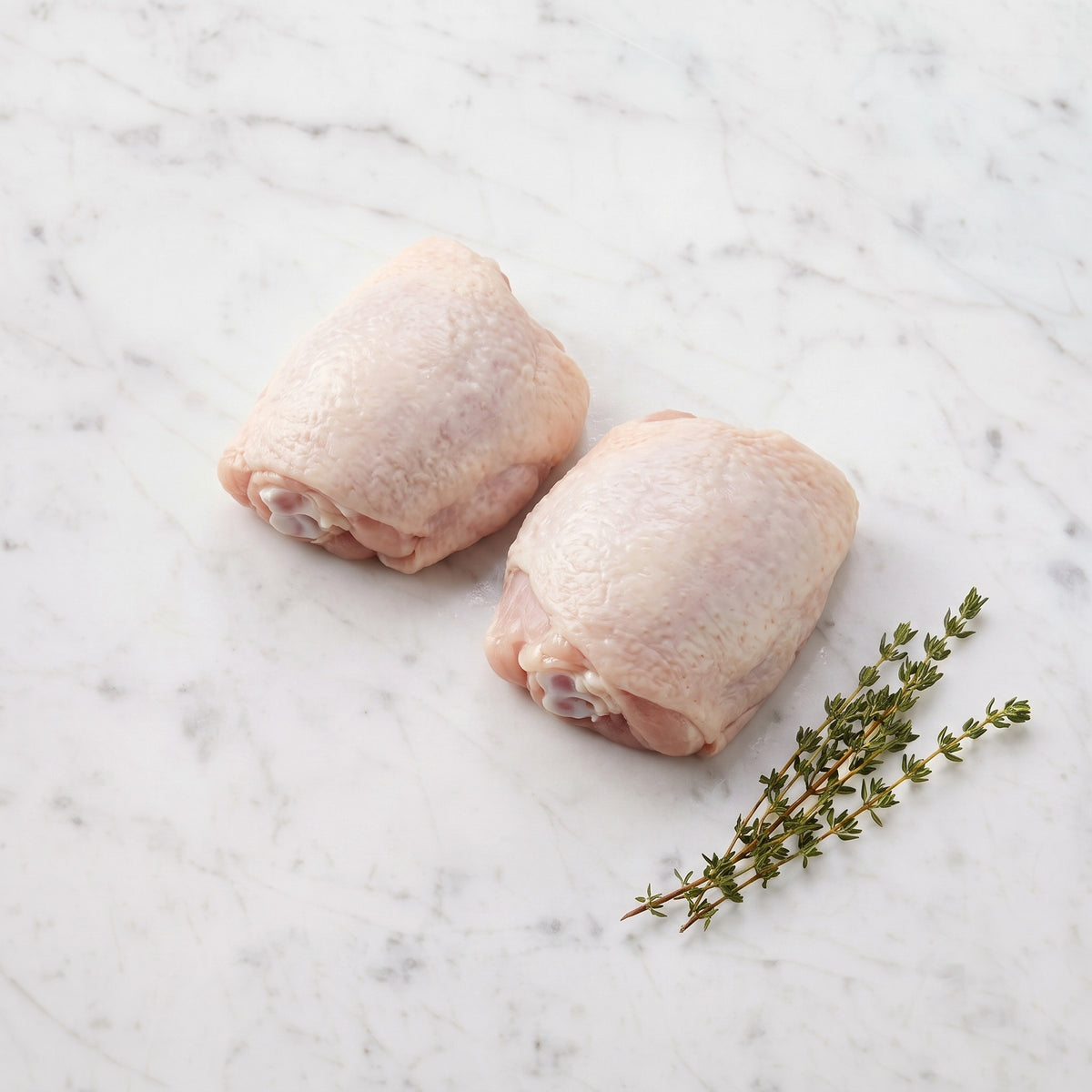 Two raw bone-in, skin-on chicken thighs with thyme sprigs on white marble