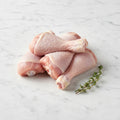 Stack of raw chicken drumsticks with a thyme sprig on white marble