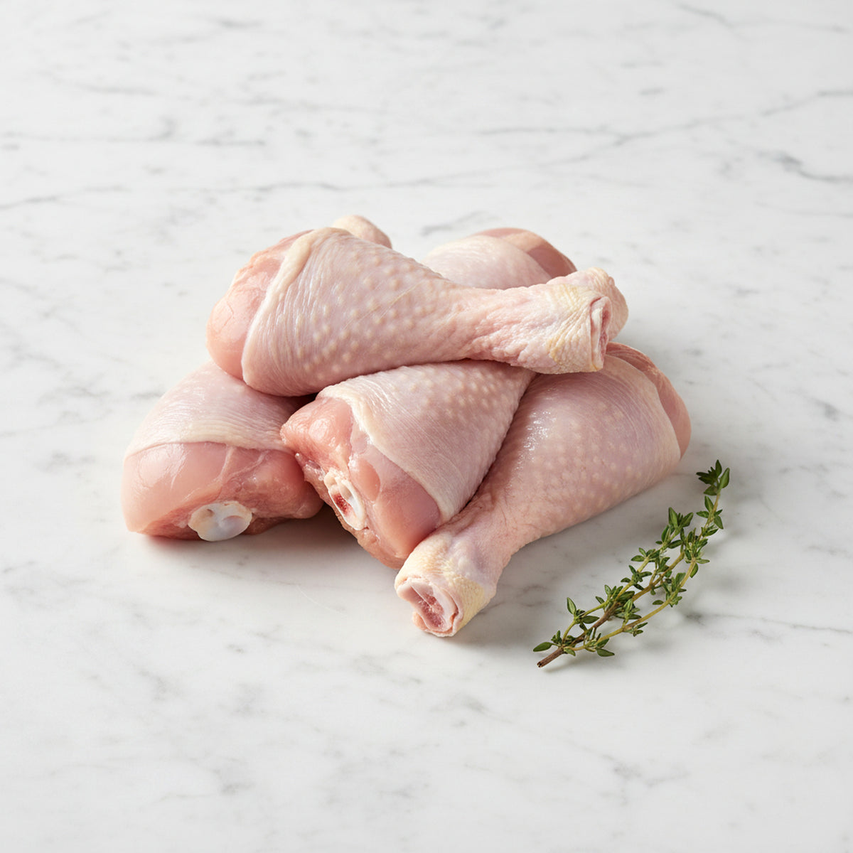 Stack of raw chicken drumsticks with a thyme sprig on white marble