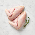 Two raw bone-in chicken breasts with wings attached and a thyme sprig on white marble