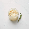 Glass jar of rendered chicken fat beside a thyme sprig on white marble
