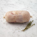 Raw netted chicken roll with cracked pepper and thyme sprigs on white marble