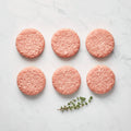 Six raw ground chicken slider patties in two rows with a thyme sprig on white marble