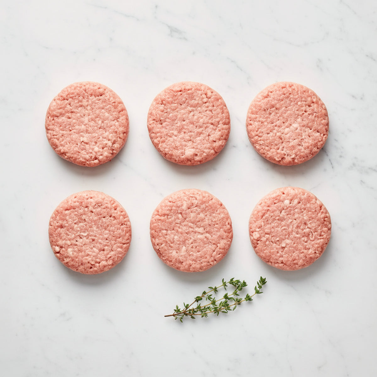 Six raw ground chicken slider patties in two rows with a thyme sprig on white marble