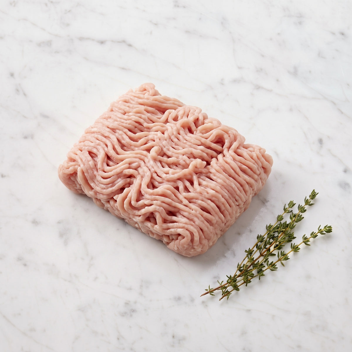 Block of raw lean ground chicken with thyme sprigs on white marble