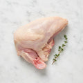Raw bone-in chicken supreme with a thyme sprig on white marble