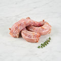Three raw chicken necks with a thyme sprig on white marble