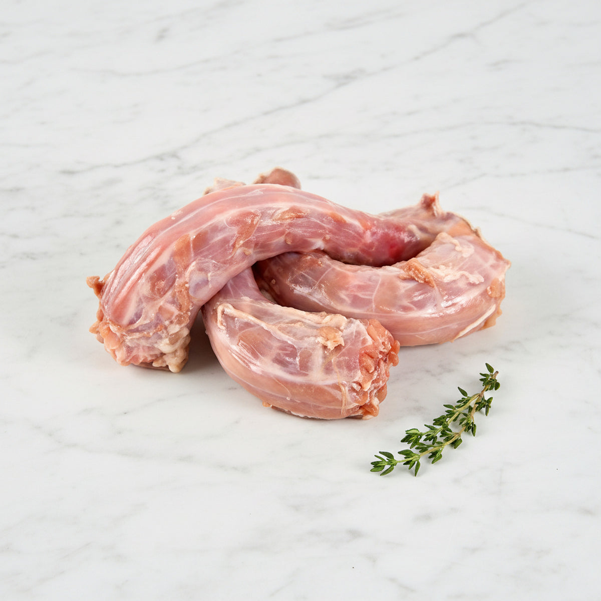 Three raw chicken necks with a thyme sprig on white marble