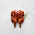 Butterflied chicken coated in glossy BBQ marinade with a thyme sprig on white marble