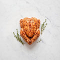 Whole raw chicken coated in roasted red pepper and garlic dry rub, with thyme sprigs on white marble