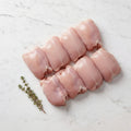 Eight raw boneless, skinless chicken legs in two rows with thyme on white marble