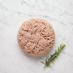 Round mound of raw lean ground turkey with a rosemary sprig on white marble