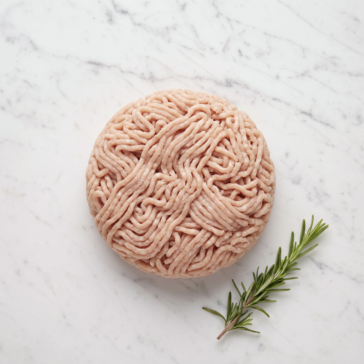 Round mound of raw lean ground turkey with a rosemary sprig on white marble