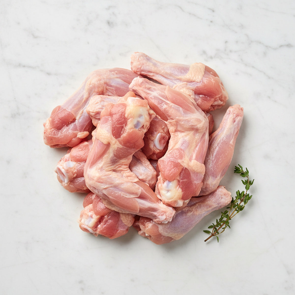 Pile of raw skinless chicken wings with a thyme sprig on white marble