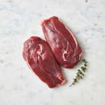 Two raw boneless duck breasts, meat side up, with thyme on white marble