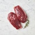 Two raw boneless duck breasts, meat side up, with thyme on white marble