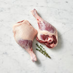 Two raw duck legs, one skin side up and one meat side up, with thyme on white marble