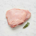 Raw skin-on turkey thigh with a thyme sprig on white marble