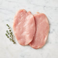 Two thin raw turkey cutlets with a thyme sprig on white marble