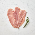 Thin raw turkey scallopini slices overlapping with a thyme sprig on white marble