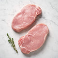 Two raw turkey steaks with a thyme sprig on white marble