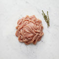 Mound of thinly sliced raw turkey for shawarma with thyme sprigs on white marble