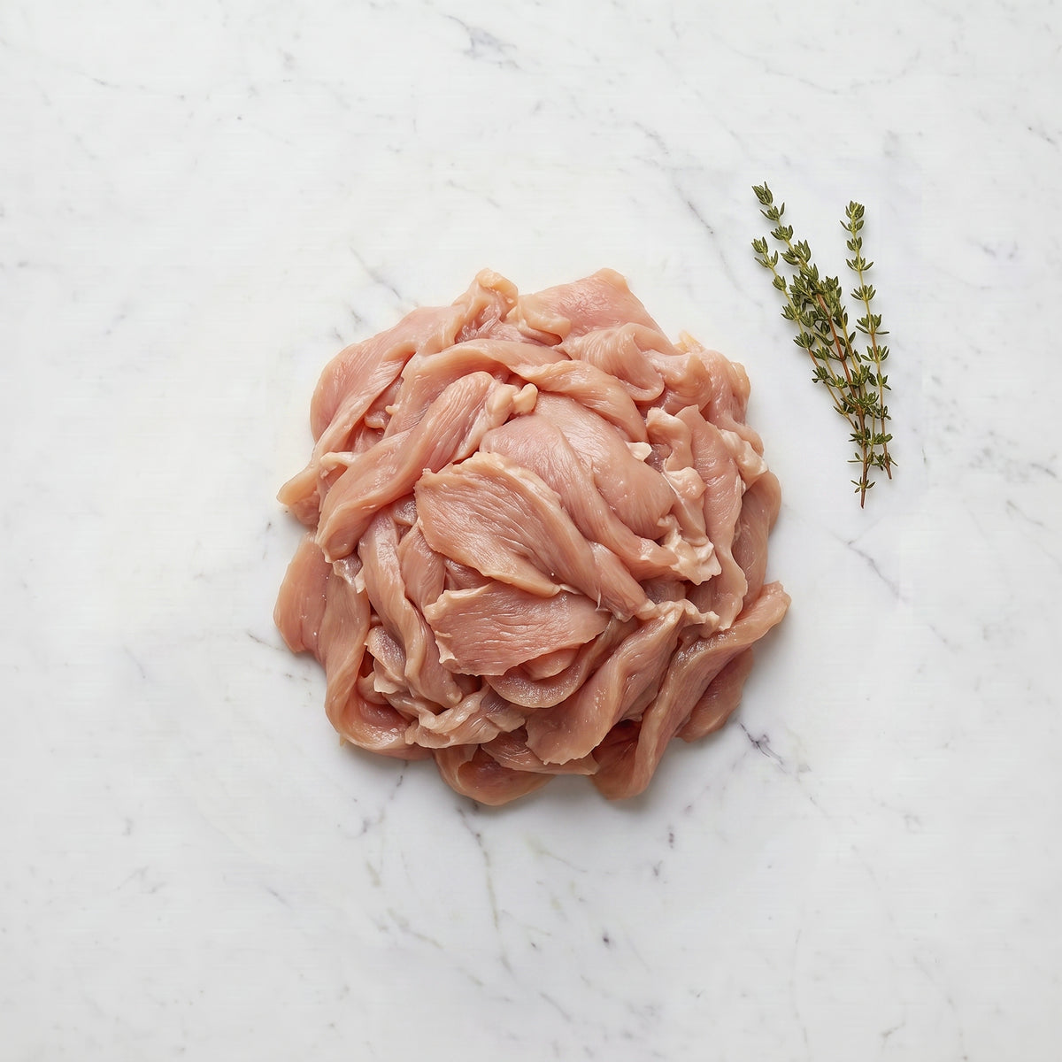 Mound of thinly sliced raw turkey for shawarma with thyme sprigs on white marble