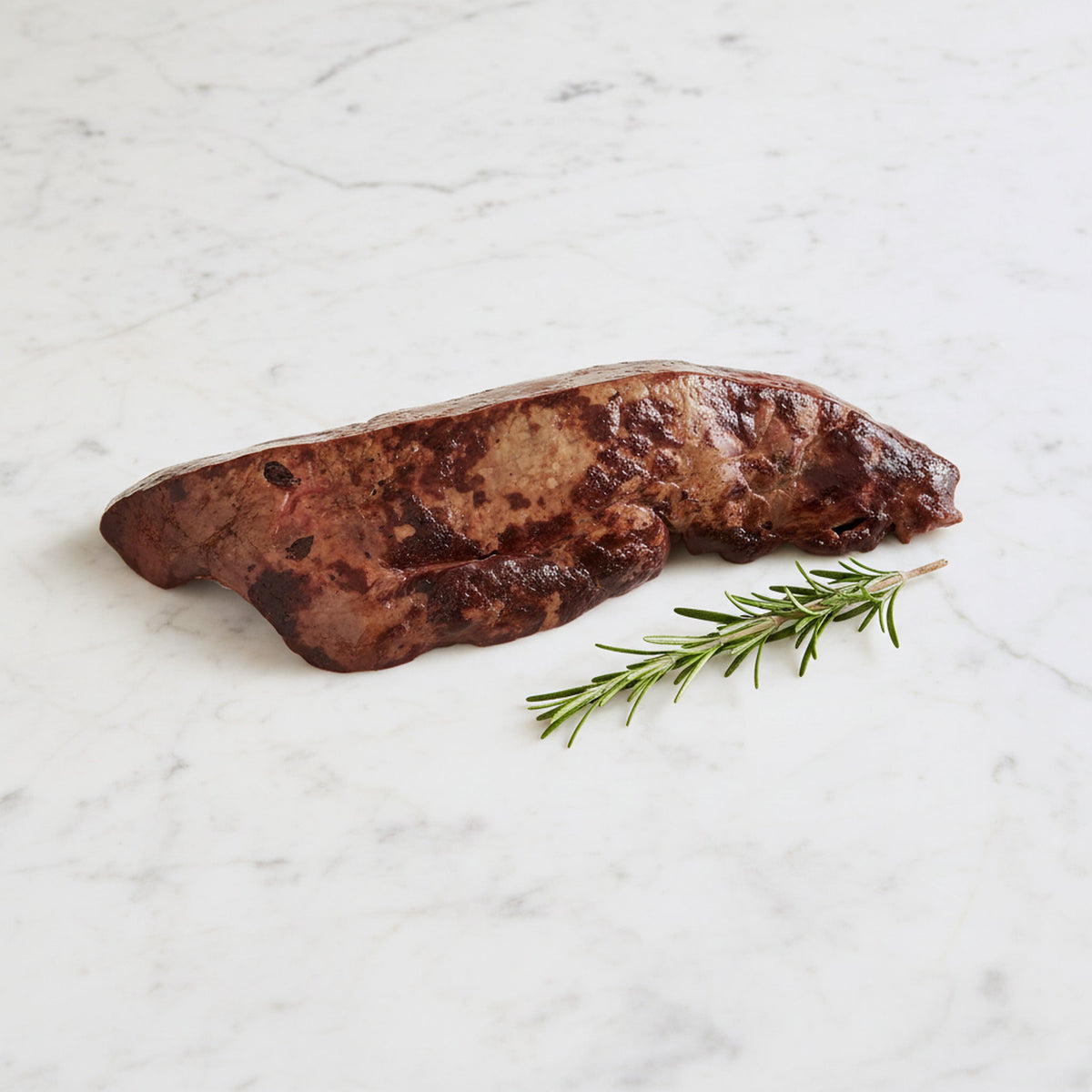 Kashered Beef Liver on a marble surface with a sprig of rosemary