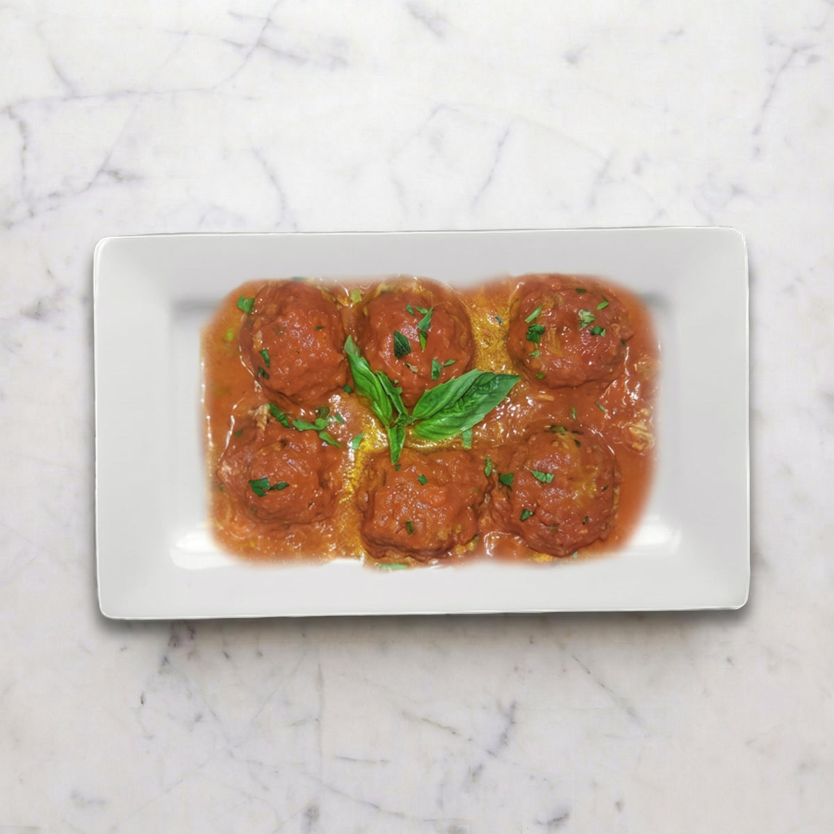 Overhead view of Beef Meatballs in Tomato Sauce on a white rectangular plate with basil