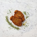 Overhead view of two pieces of Breaded Cooked Kosher Chicken Schnitzel with rosemary on a marble surface