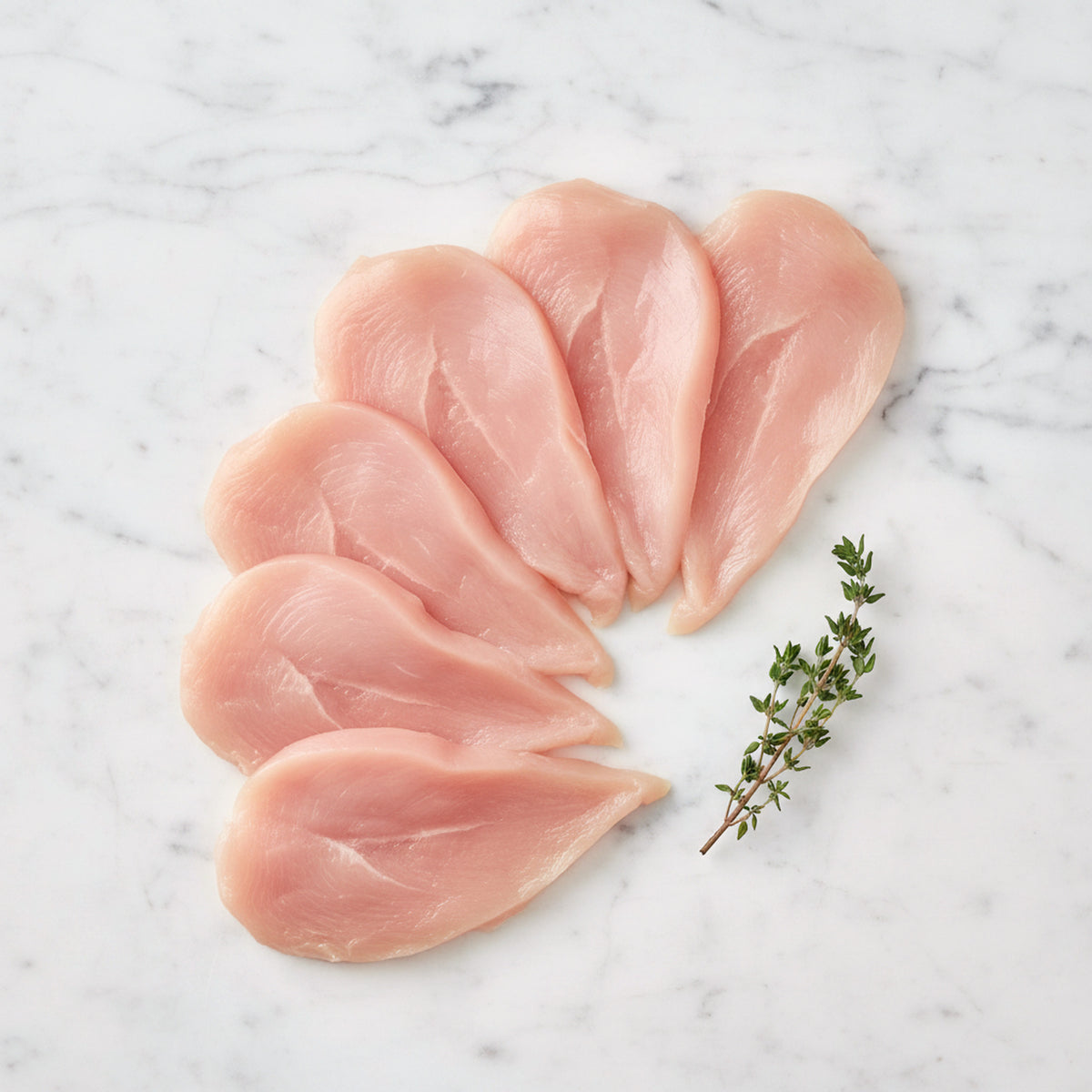 Six thin raw chicken scallopini slices on a white marble surface