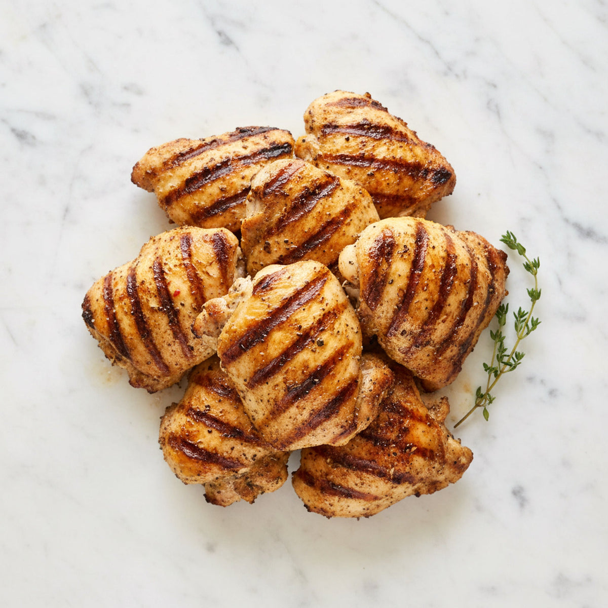 Overhead view of Grilled Boneless Chicken Legs with grill marks and thyme on a marble surface