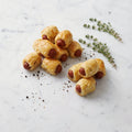 A pile of Hotdogs in Blanket, mini hot dogs wrapped in golden puff pastry, with thyme on marble