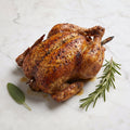 A whole Kosher Rotisserie Chicken with crisp seasoned skin, rosemary and sage on a marble surface
