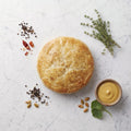 Overhead view of a round Potato Knish with golden pastry, thyme and a bowl of mustard on marble