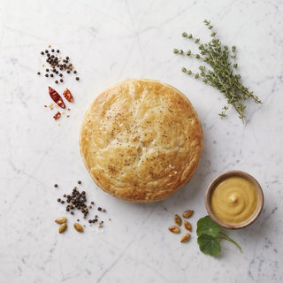 Overhead view of a round Potato Knish with golden pastry, thyme and a bowl of mustard on marble