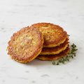 A stack of golden Potato Latkes with a sprig of thyme on a marble surface