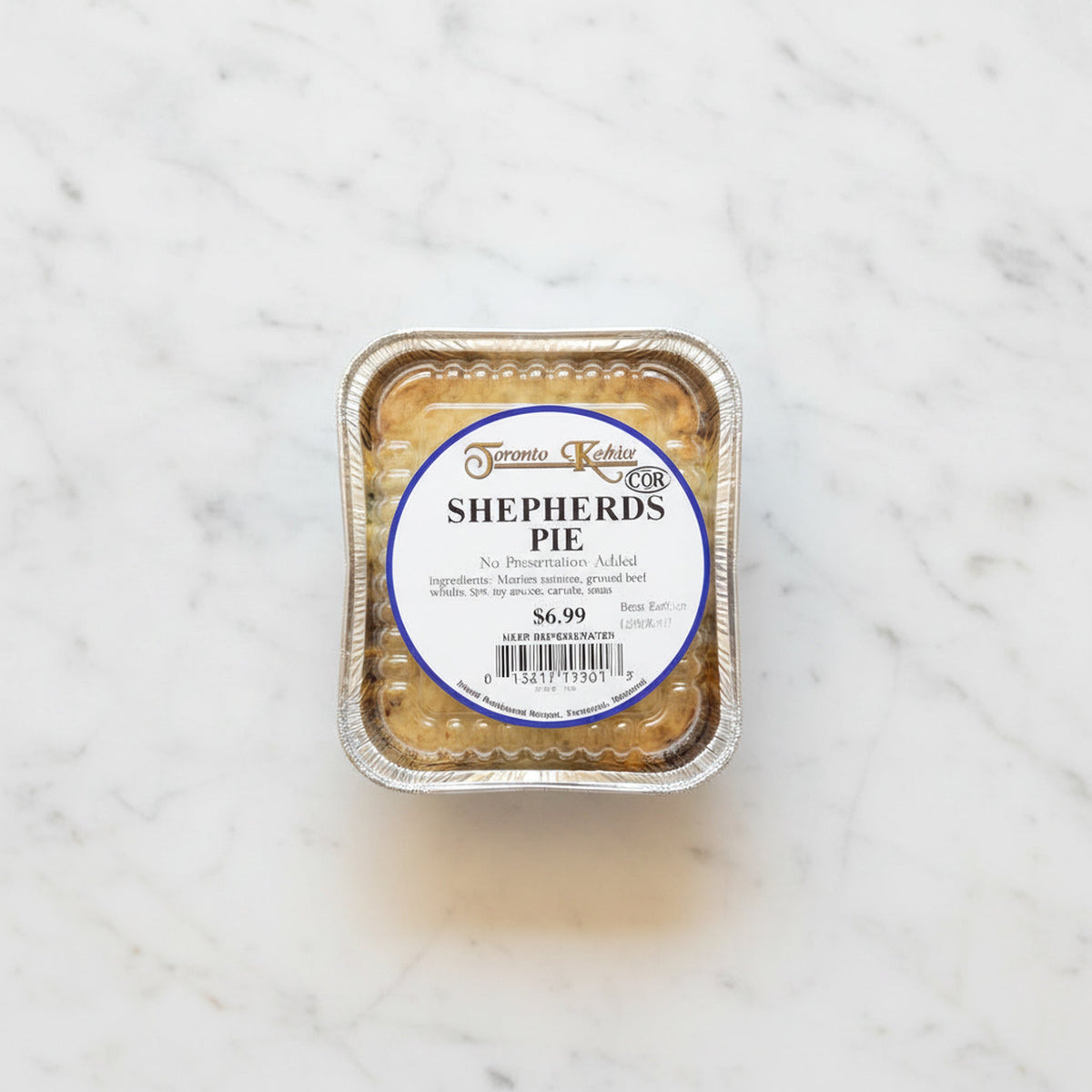Overhead view of a Shepherd's Pie in a foil tray with a Toronto Kosher label, on a marble surface