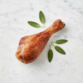 A Smoked Turkey Drumstick with glossy mahogany skin and sage leaves on a marble surface