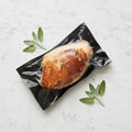 A Smoked Turkey Half Breast in vacuum packaging with sage leaves on a marble surface