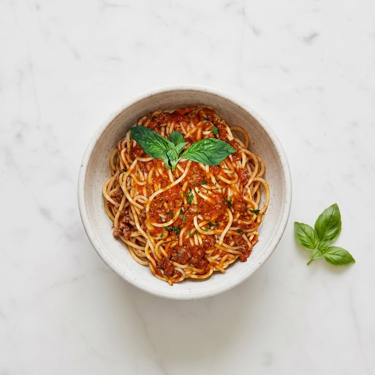 Overhead view of a bowl of Spaghetti with Meat Sauce, garnished with fresh basil, on marble