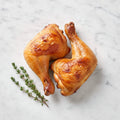 Overhead view of two TK BBQ or Roasted Chicken Legs with golden skin on a marble surface