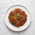 Overhead view of TK Beef Stir Fry with Asian Noodles, red pepper and scallion on a white plate
