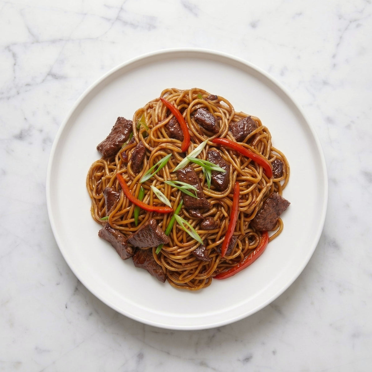 Overhead view of TK Beef Stir Fry with Asian Noodles, red pepper and scallion on a white plate