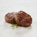 Two TK Char Broiled Beef Burgers with grill marks and a sprig of rosemary on a marble surface