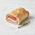A TK Deli Roll sliced to show layers of deli meat in golden pastry, with thyme on a marble surface